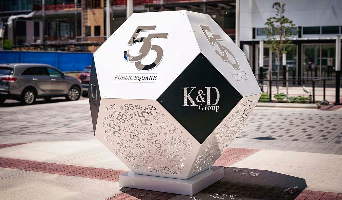 Contemporary polyhedron-shaped public art featuring the logos of 55 Public Square and K&D Group in the city square