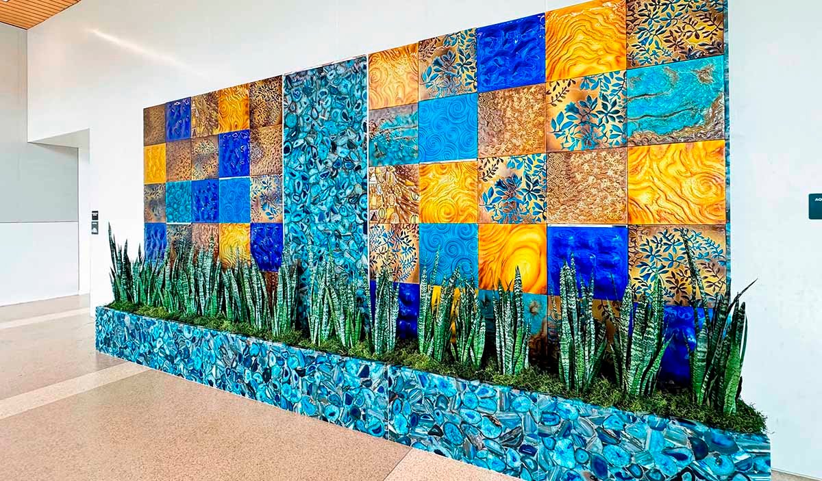 An art glass installation in shades of blue, turquoise and gold with plants at the base