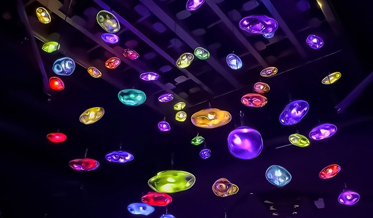 A kinetic installation featuring multicolored glowing elements suspended from the ceiling.