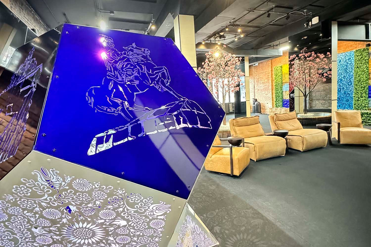 Showroom of SKYFORM STUDIO with designer installation featuring engraved blue metal panels, modern lounge chairs, and decorative art walls with greenery.