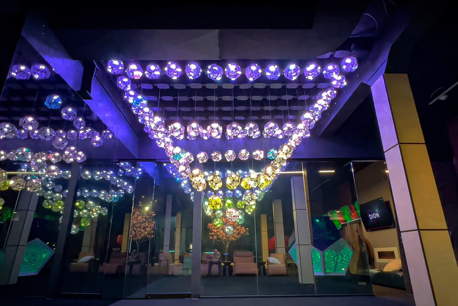 Kinetic light installation in SKYFORM STUDIO showroom, ceiling structure with glowing crystal-like spheres creating colorful reflections.