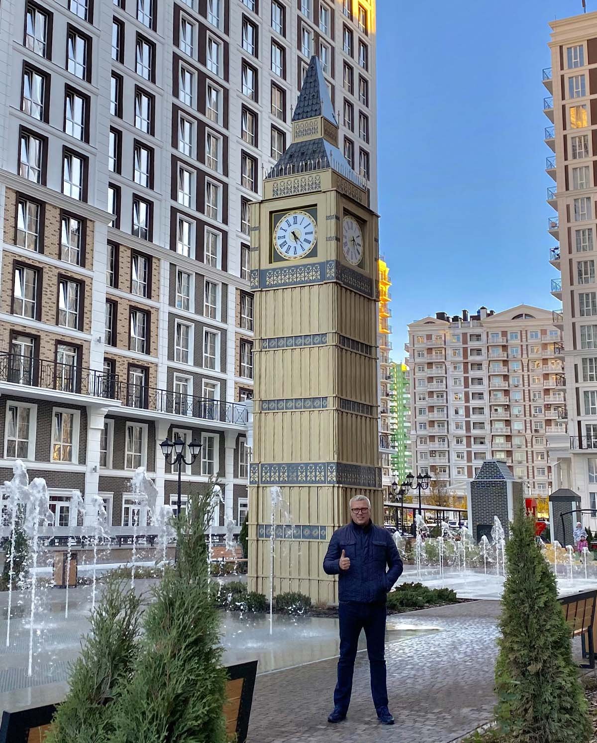 Public art in the form of a miniature copy of Big Ben in front of a fountain with the artist in the courtyard of a modern residential complex