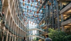 Floating Fleet kinetic installation beneath the glass roof of a multi-level airport atrium, where dozens of airships and balloon-like vessels float above visitors.