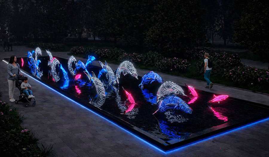 Public art installation “Water World” featuring illuminated dolphin and fish sculptures in an interactive water basin at night in a park setting.