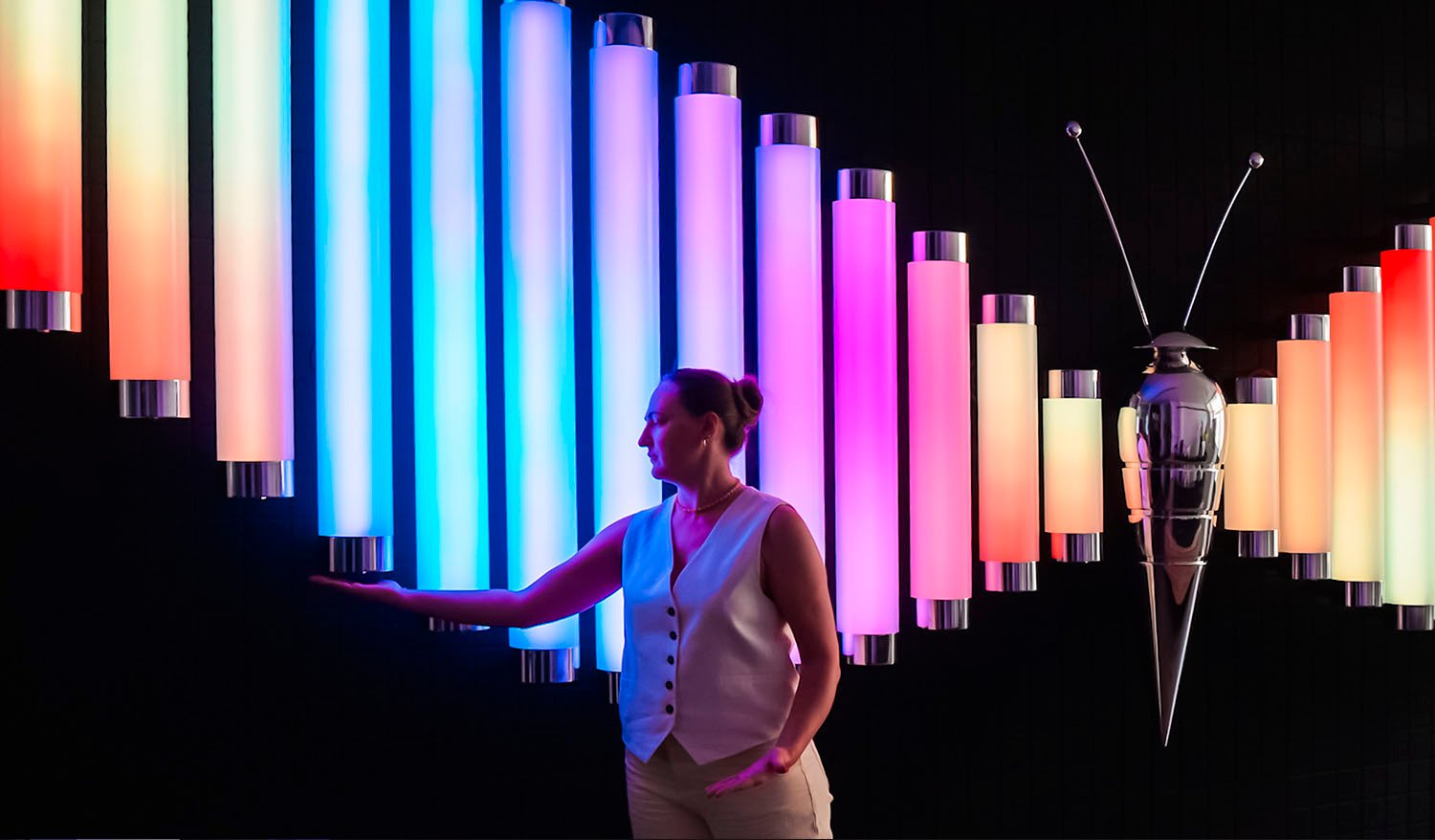 Visitor interacting with the Butterfly installation featuring colorful illuminated tubes and a metallic butterfly sculpture.