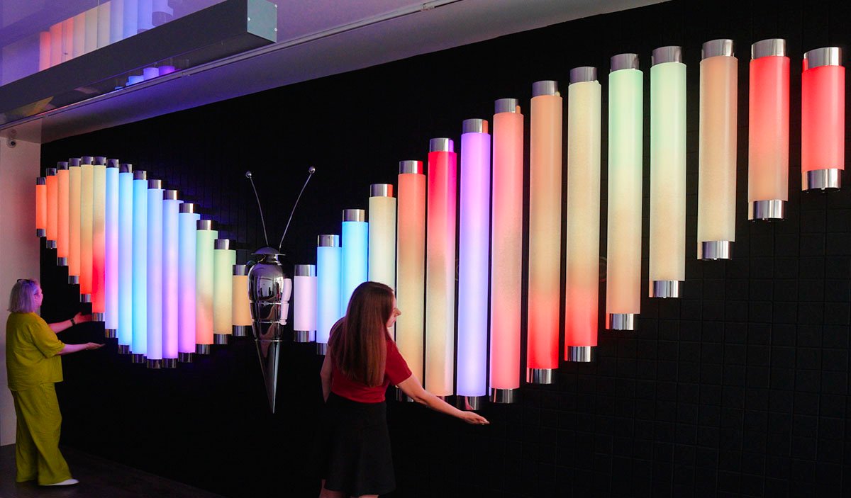 Two visitors interacting with the Butterfly installation featuring wings made of colorful illuminated tubes.