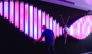 زائر يتفاعل مع تركيب «Butterfly» المكوّن من أنابيب ضوئية عمودية متوهجة باللونين الوردي والأبيض.