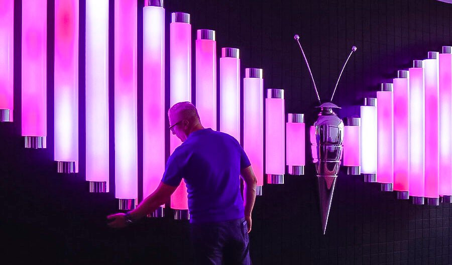 Visitor interacting with the Butterfly installation featuring glowing pink and white vertical light tubes.